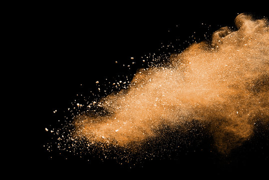 Abstract brown powder explosion. Closeup of brown dust particle splash isolated on black background