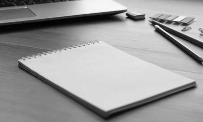An open notebook for notes, pencils, markers, a pen, a pot with cactus, a notebook and paper clips on a wooden background (office desk).