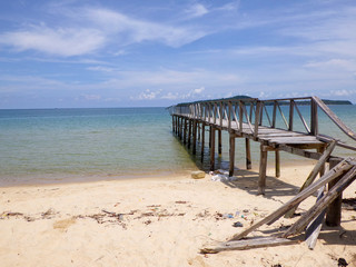 an empty wooden port at a sandy beach of an island at a bright sunny day