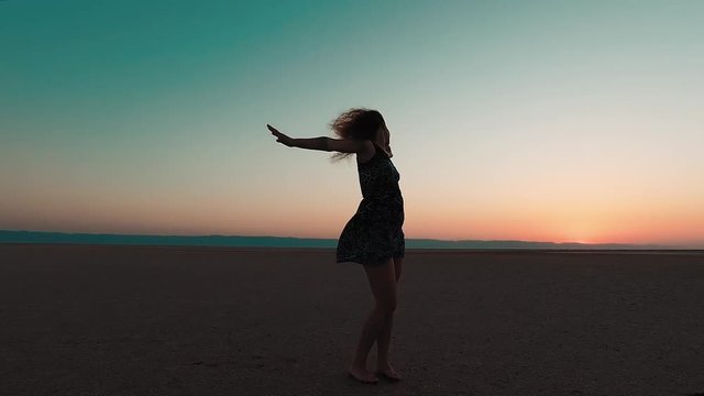 The young girl dances in the desert, at sunrise the sun.