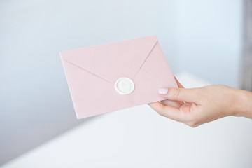 Close-up photo of female hands holding invitation envelope with a wax seal, a gift certificate, a...