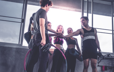 Happy young athletic people in sportswear putting hand together in the gym