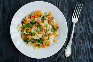Italian pasta in a sauce with shrimps on a plate, top view. Dark wooden background.