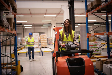 Warehouse worker in forklift handling palette with goods in storage area. Industrial worker...