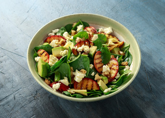 Summer Peach Salad with spinach, avocado, walnuts and feta cheese in rustic bowl. healthy food.