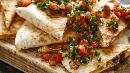 Mexican food quesadillas with chicken and cheese served on rustic wooden chopping board with homemade fresh salsa topping