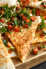 Mexican food quesadillas with chicken and cheese served on rustic wooden chopping board with homemade fresh salsa topping