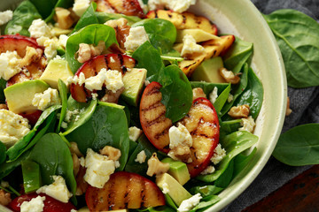 Summer Peach Salad with spinach, avocado, walnuts and feta cheese in rustic bowl. healthy food.
