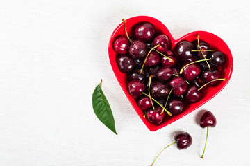 Cherries in Heart Shaped Bowl on White Wooden Background. Selective focus.