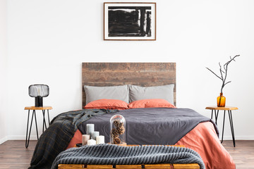 King size bed with orange and grey bedding between two wooden nightstand with lamp and vase