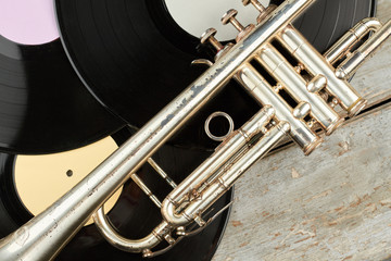 Naklejka premium Trumpet and vinyl records close up. Old rusty trumpet with long play vinyl discs on wooden boards. Retro instrument of classical music.