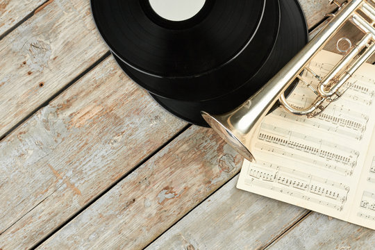 Retro musical objects and copy space. Vinyl records, trumpet and musical notes on wooden background.