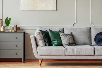 Pillows on long comfortable living room couch in grey scandinavian style interior with wooden floor