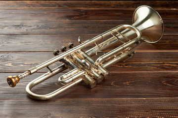 Shiny trumpet on brown wooden background. Classical trumpet on dark wooden surface. Vintage instrument of jazz music.