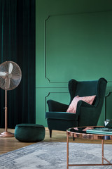 Emerald green velvet armchair with pastel pillow in trendy living room interior with copper accents
