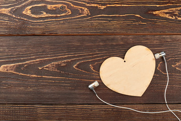 Earphones, wooden heart and copy space. Plywood heart and earphone on brown wooden background. Listen music with heart.