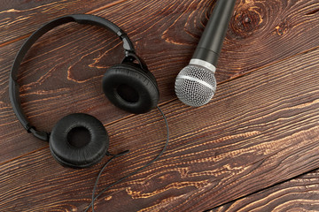 Microphone and headphones on brown wooden background. Gray microphone and black headphones on brown wooden table. Modern audio technologies.