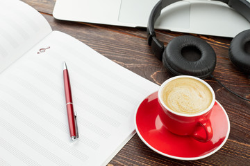 Musical papers, headphones and red cup. Blank notebook for musical notes, pen, laptop, headphones and blank coffee cup. Song writer work place.