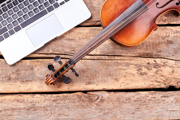 Laptop and violin on wooden planks. Classic musical instrument in vintage style. Retro and modern musical technology.