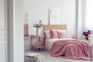 Pastel pink pillow and blanket on single wooden bed with white bedding in scandinavian bedroom...