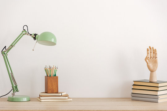 Pastel mint colored lamp on wooden desk with books, copy space on empty white wall
