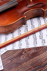 Violin, bow and musical notes sheets. Brown violin and musical notes on wooden surface, vertical...