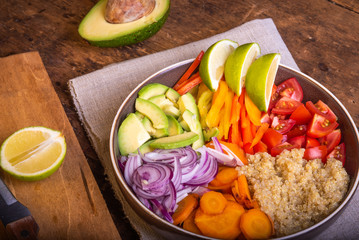 Salad bowl with quinoa; carrots; avocado; onion; pepper; tomato with slices of lime close-up - vegetarian dish; buddha bowl