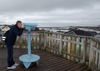 middle aged man using sightseeing binoculars on top of a hill overlooking the harborfront of Saint...