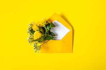 Yellow roses and white Gypsophila in envelope close-up on vivid yellow background. Top view, flat lay. Template for greeting card. Festive floral background