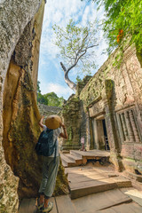 Fototapeta premium One tourist visiting Angkor ruins amid jungle, Angkor Wat temple complex, travel destination Cambodia. Woman with traditional hat, rear view.