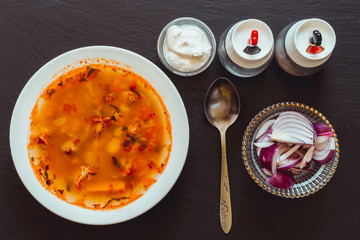 Bean soup with smoked bone served with sour cream and red onion – Food background with spices and vegetables on dark slate