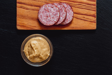 Salami slices on a wooden cutting board next to seasoning – Pork meat product served at breakfast...