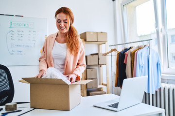 Young online store owner packing delivery into cardboard box in office