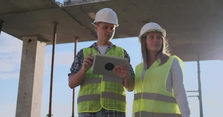 Supervisor of a building under construction man discussing with engineer designer woman the progress of construction and examines a building plan