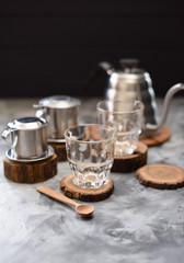 Equipment for making drip coffee Vietnamese style: phin, goose neck kettle and glasses on dark background