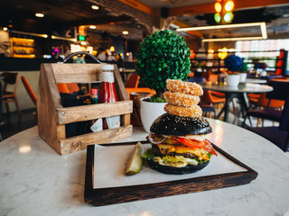 Big burger with beef cutlet, black bun, onion rings
