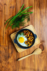 Fried eggs with mushrooms in a cast iron pan. Traditional dish of russian cuisine.