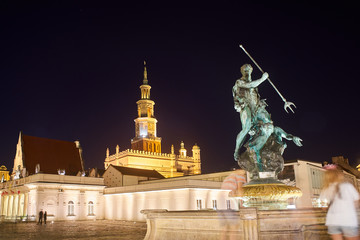 Obraz premium A fountain with a sculpture of Neptune and a tower of the town hall at night in the city of Poznan.