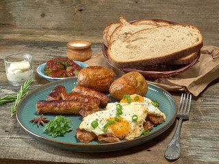 Fried sausages with potatoes,scrambled eggs and bacon.On wooden background