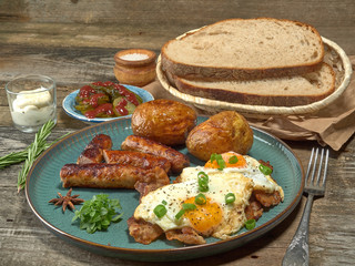 Fried sausages with potatoes,scrambled eggs and bacon.On wooden background