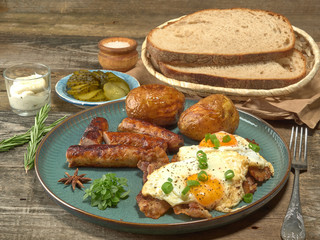 Fried sausages with potatoes,scrambled eggs and bacon.On wooden background