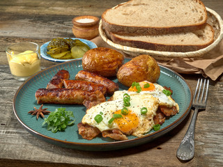 Fried sausages with potatoes,scrambled eggs and bacon.On wooden background
