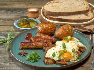 Fried sausages with potatoes,scrambled eggs and bacon.On wooden background