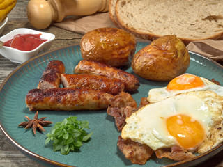 Fried sausages with potatoes,scrambled eggs and bacon.On wooden background