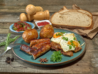 Fried sausages with potatoes,scrambled eggs and bacon.On wooden background