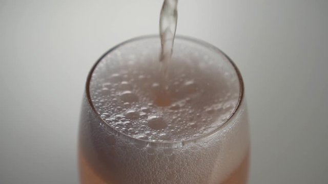 A soft, slow stream of drink falls into a glass filled with liquid and foam. Bubbles appear and burst with splashes