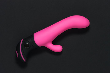 Sex toys on a black background. Sex gadget and masturbation device. A pink rubber and silicone dildo is lying on black paper. View from above. Place for text. Flat lay. Sex shop concept.