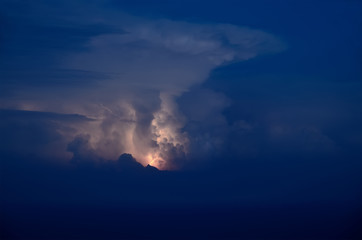 lightning shines in the clouds above the sea at night