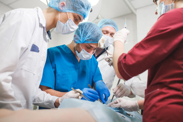 Group of surgeons at work operating in surgical theatre. Resuscitation medicine team wearing protective masks holding steel medical tools saving patient. Surgery and emergency concept.