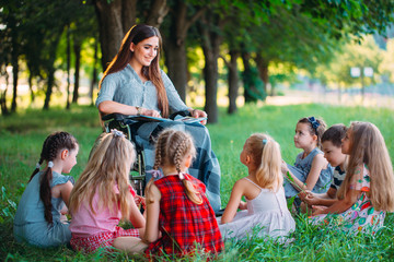 Disabled teacher conducts a lesson with children in nature. Interaction of a teacher in a wheelchair with students.